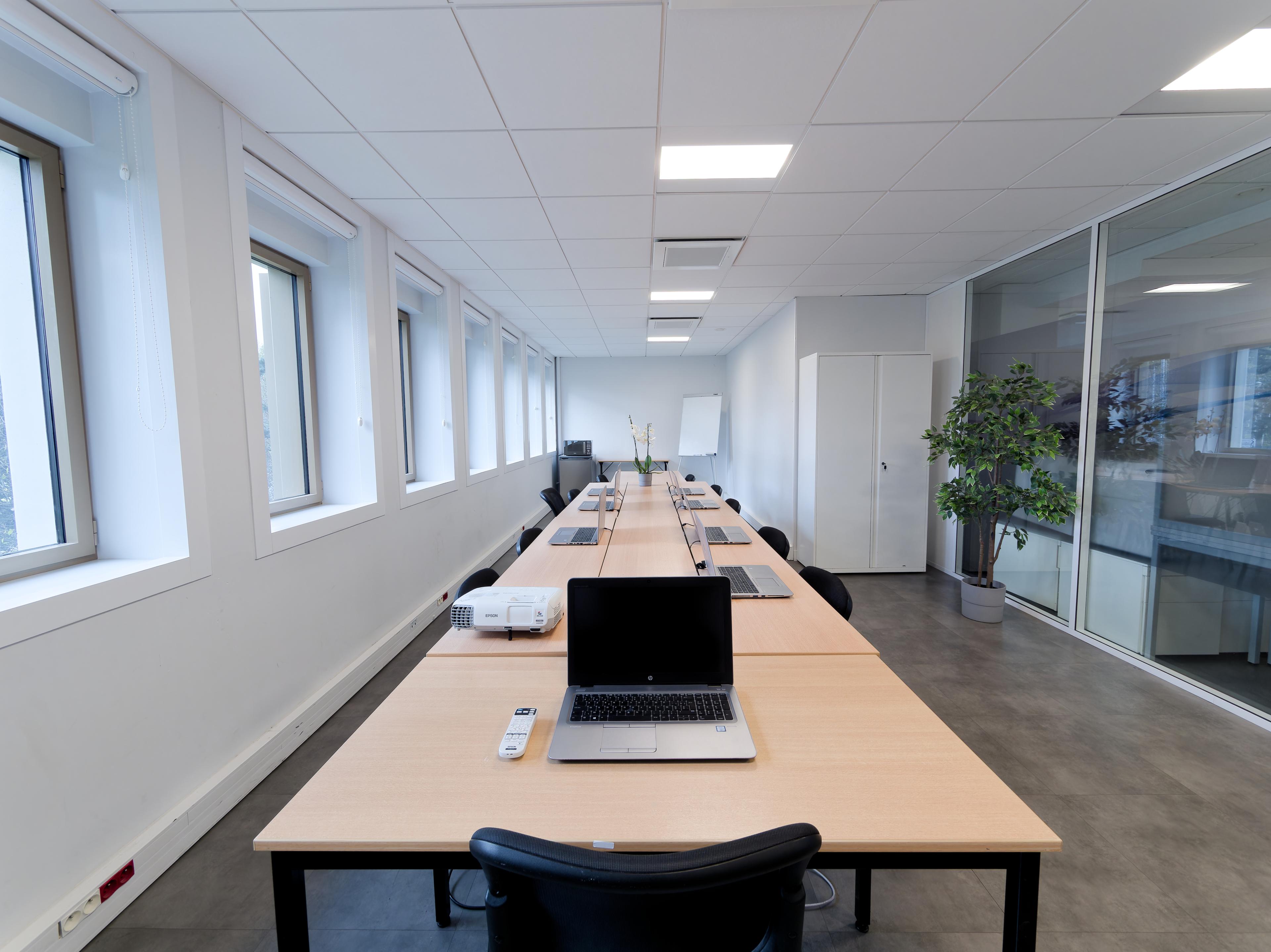 Salle de réunion équipée avec grande table, ordinateurs et vidéoprojecteur